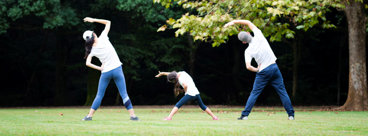 A mother and a father exercising in the park with their child